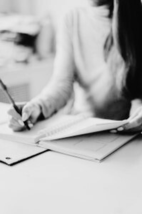 Person writing in a notebook while referencing another document, focusing on work or study.