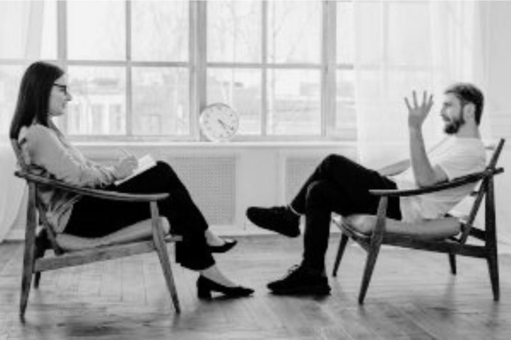 A woman and a man having a discussion while seated in chairs facing each other in a bright, modern office setting.