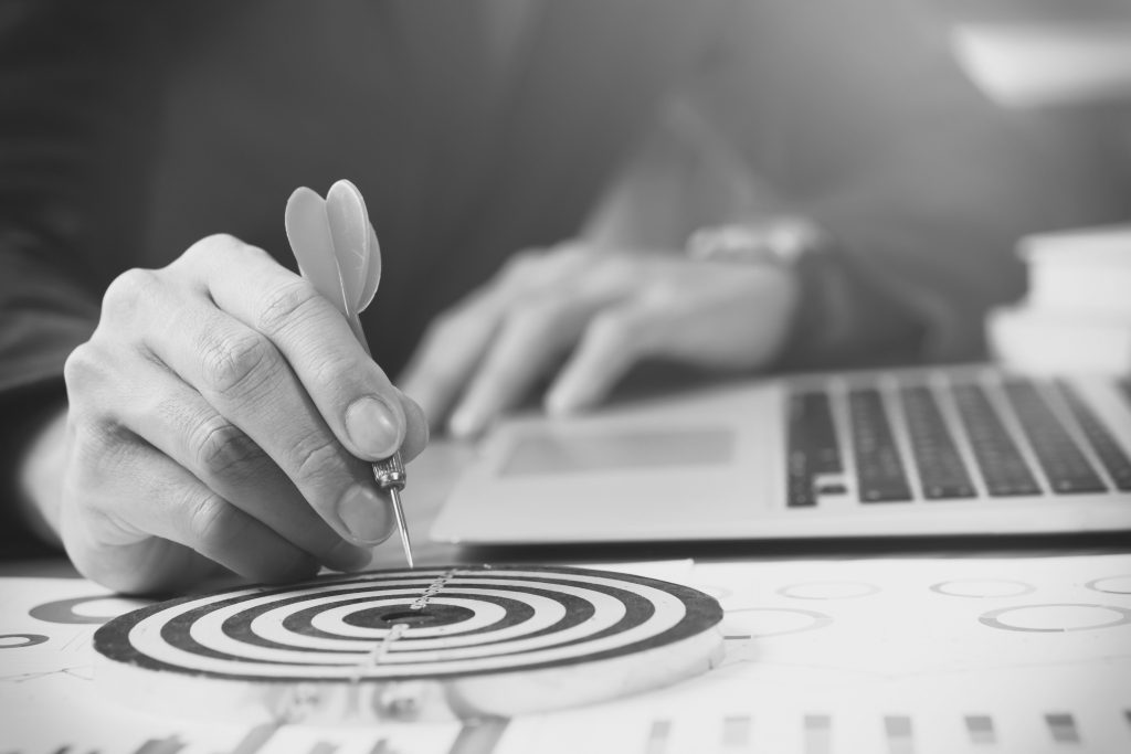 A hand holding a dart aimed at a target, representing focus on key business outcomes rather than outputs.